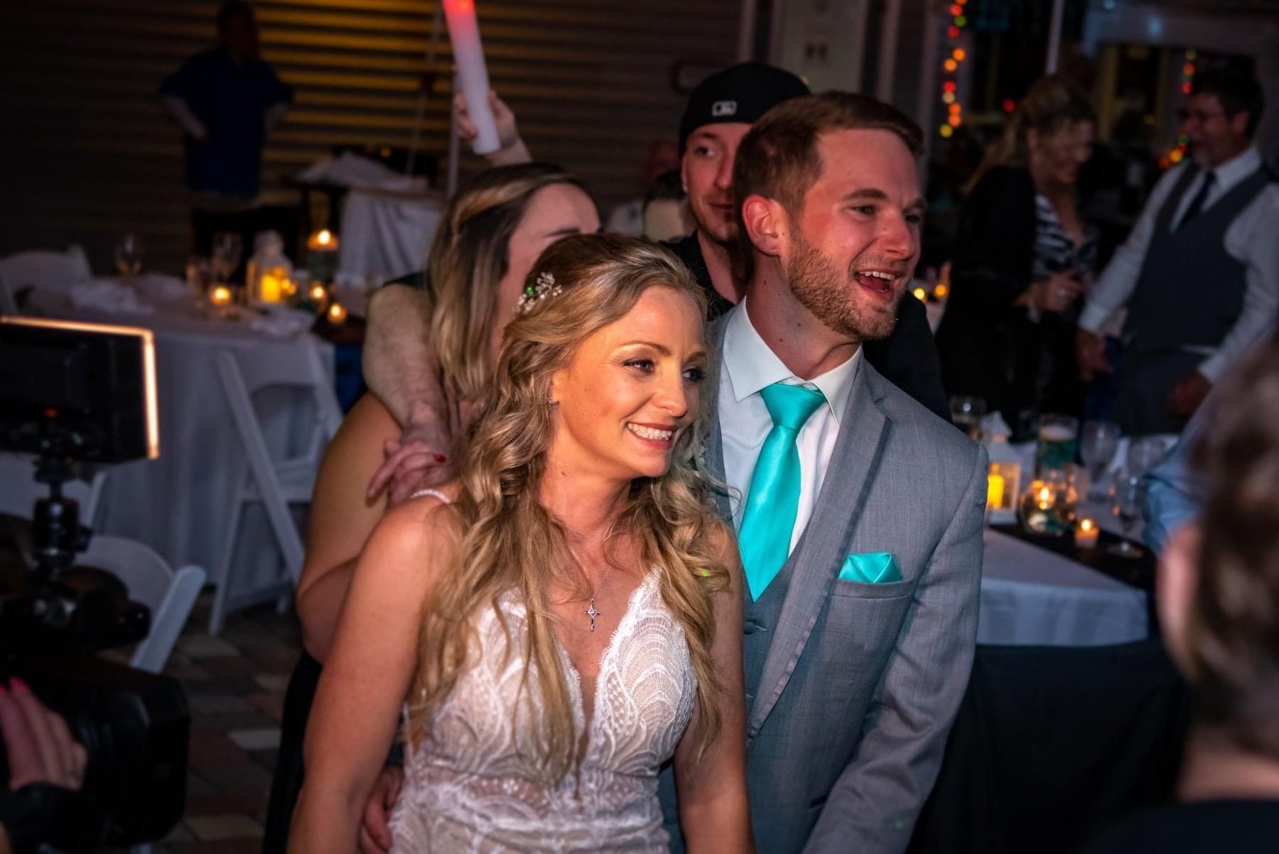 A smiling bride and groom stand close together at their warmly lit evening wedding reception.